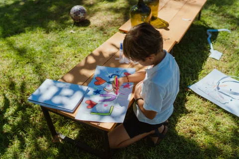 Persona dibuja con un marcador sobre una lámina colorida en una mesa exterior de madera.