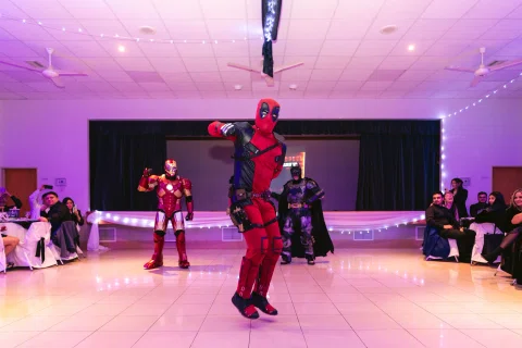 Persona con disfraz rojo y negro se mueve por la pista mientras otras figuras disfrazadas aparecen al fondo.
