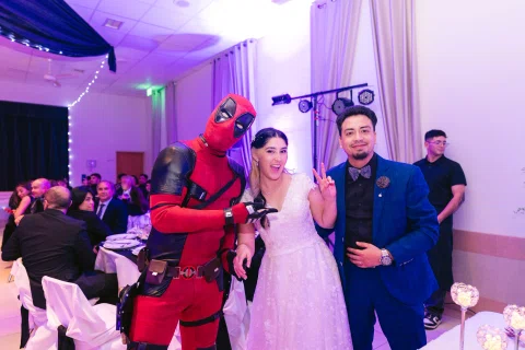 Persona con disfraz rojo y negro posa junto a una mujer con vestido blanco y un hombre con traje azul.