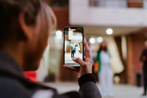 Persona fotografía con un celular a una mujer con blazer verde en un espacio interior.