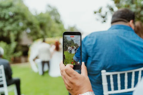 Persona sostiene un teléfono para grabar a dos personas desenfocadas al fondo.