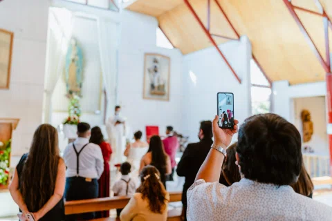 Persona levanta un teléfono dentro de una iglesia mientras varias personas permanecen sentadas frente al altar.
