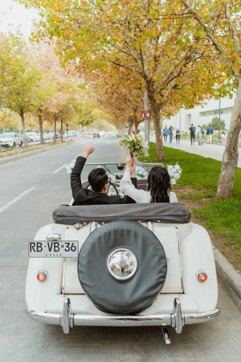 Persona levanta una mano desde un automóvil convertible blanco visto desde atrás.