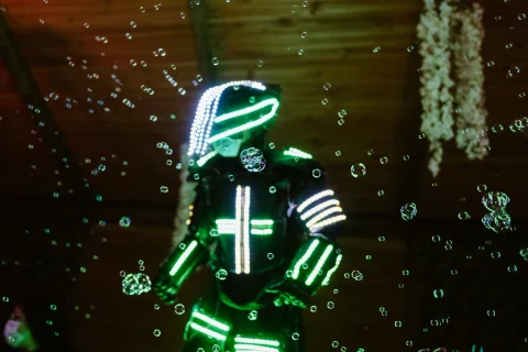 Persona con traje iluminado en verde rodeada de burbujas sobre un fondo oscuro.