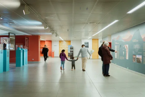 Varias personas caminan por un pasillo interior con paneles de exhibición en las paredes.