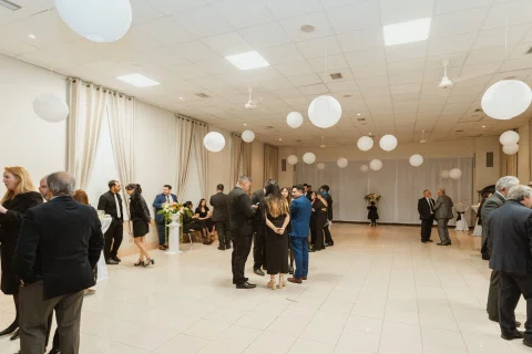 Varias personas permanecen reunidas y conversando en un salón decorado con globos blancos.
