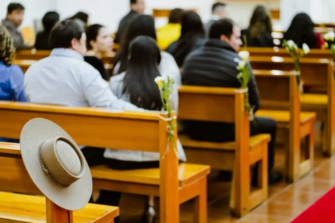 Personas sentadas en bancos de una iglesia, con un sombrero tradicional apoyado en primer plano.