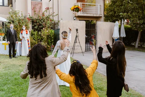 Ramo de flores vuela por el aire sobre una mujer con vestido blanco de espaldas, mientras tres mujeres levantan los brazos en primer plano.