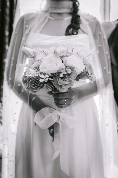 Ramo de flores sostenido frente a un vestido blanco, en una fotografía en blanco y negro.