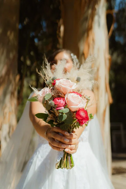 Ramo de rosas rosadas y rojas en primer plano, con una mujer con vestido blanco desenfocada detrás.
