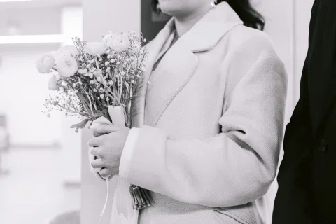 Detalle en blanco y negro de un ramo sostenido por una persona con traje claro.