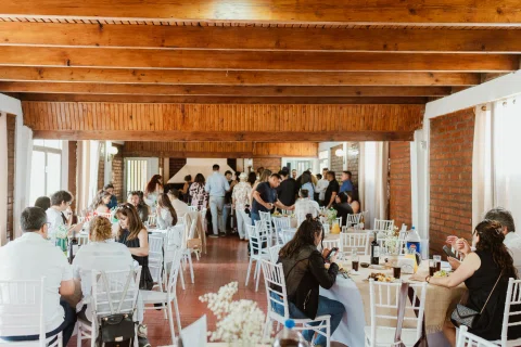 Salón con mesas y sillas bajo vigas de madera y muros de ladrillo.