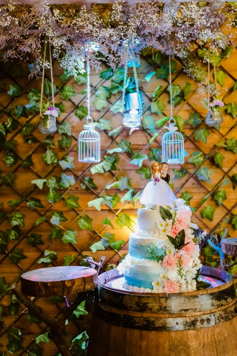 Torta decorada con figuras y flores sobre una mesa iluminada.