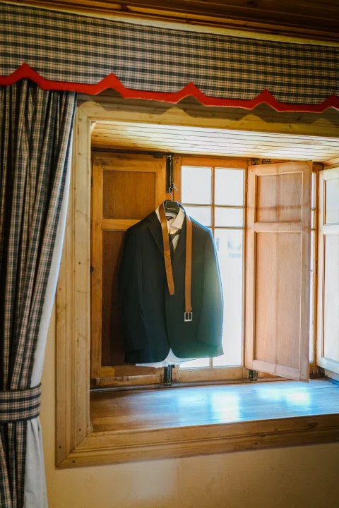 Traje oscuro colgado frente a una ventana de madera.