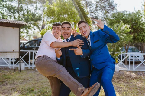 Tres hombres posando de forma lúdica en el jardín durante la celebración.