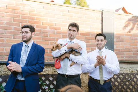 Tres hombres posan juntos; el del centro sostiene un perro pequeño.