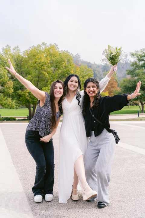 Tres mujeres levantan los brazos mientras posan juntas al aire libre.
