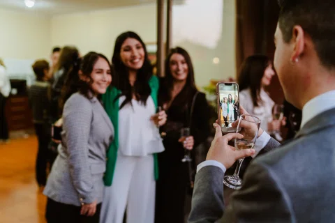 Tres mujeres posan juntas mientras una persona las fotografía con un celular.