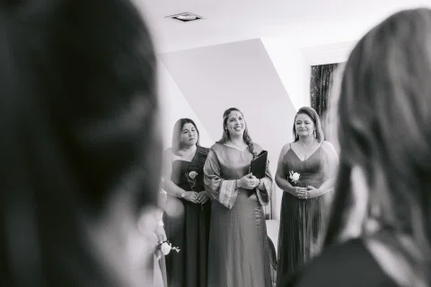 Tres mujeres se reflejan en un espejo mientras otra mujer aparece desenfocada en primer plano.