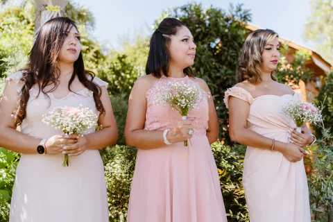 Tres mujeres con vestidos rosados sosteniendo pequeños ramos durante la ceremonia.