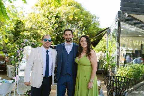 Dos hombres y una mujer posan juntos en un jardín; uno de los hombres viste traje azul.