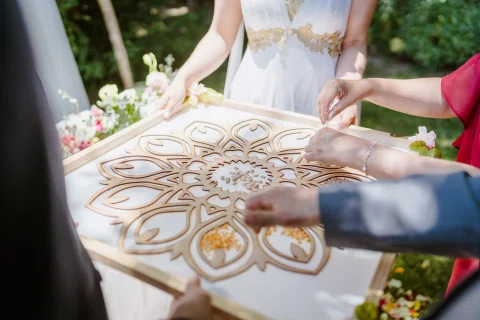 Varias manos rodean un tablero de madera con un diseño floral geométrico durante la ceremonia.