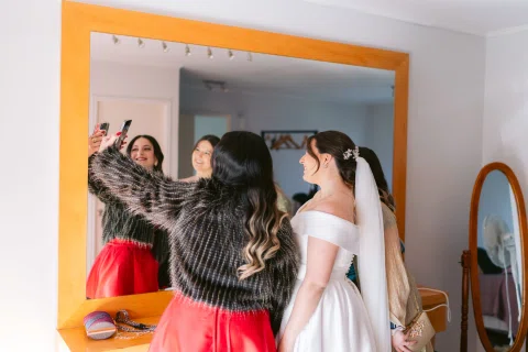 Varias mujeres posan frente a un espejo junto a una mujer con vestido blanco.