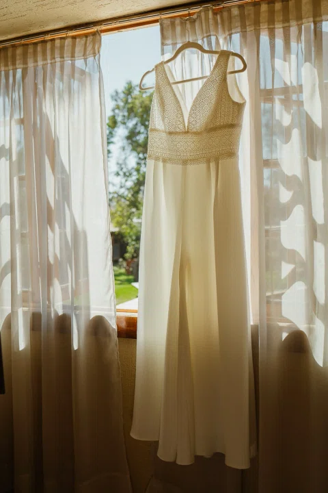 Vestido blanco colgado frente a una ventana, con la silueta iluminada por la luz exterior.