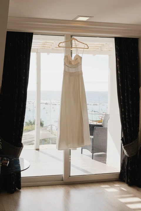 Vestido blanco colgado frente a un ventanal iluminado.