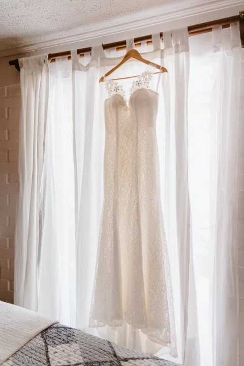 Vestido blanco colgado frente a una ventana entre cortinas claras y luz suave.
