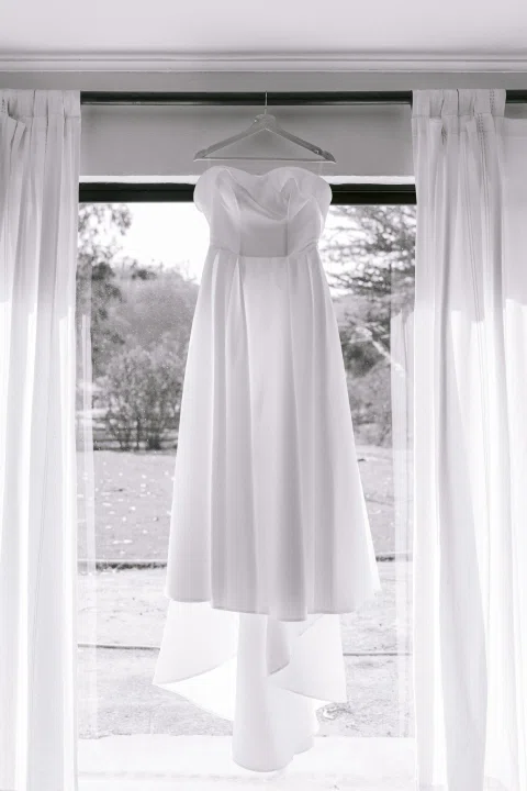 Vestido blanco largo cuelga frente a una ventana en una fotografía en blanco y negro.