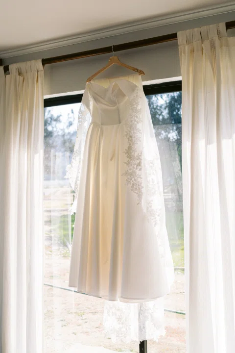 Vestido blanco largo cuelga frente a una ventana iluminada.