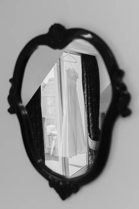 Vestido blanco colgado junto a un ventanal, reflejado en un espejo.
