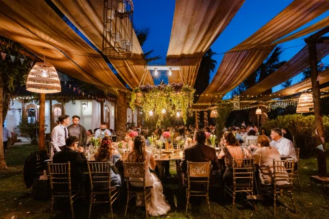 Vista amplia de la cena con mesas bajo un toldo de madera y luces cálidas.