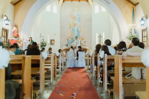 Vista general del interior de una iglesia con un pasillo rojo y personas sentadas a ambos lados.