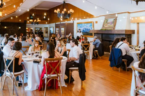 Vista general de un salón con varias personas sentadas alrededor de mesas.