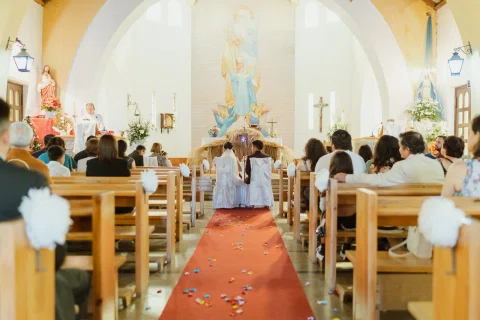 Vista del pasillo rojo de una iglesia con un hombre y una mujer sentados frente al altar al fondo.