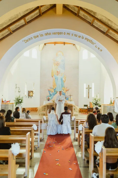 Vista vertical del interior de una iglesia desde el fondo, con personas sentadas y el altar al frente.