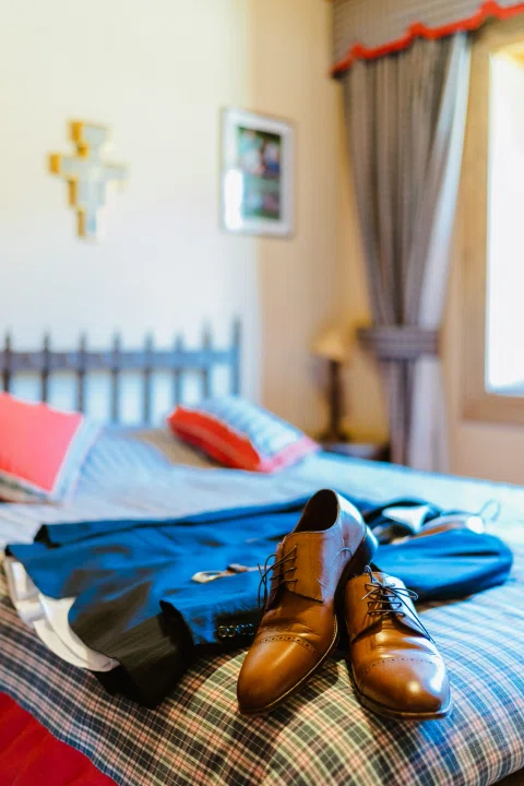 Zapatos de cuero marrón y prendas de un traje azul dispuestos sobre una cama.